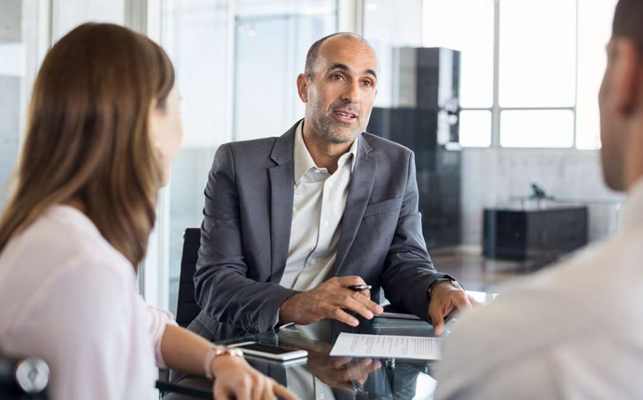 The Image Depicts A Business Advisor Engaged In A Conversation With Two Clients, Offering Business Strategy Consulting And Advisory Services. The Advisor Holds A Pen In His Right Hand, Demonstrating Attentiveness While Actively Listening To The Clients, Who Appear Engaged And Involved In The Discussion.